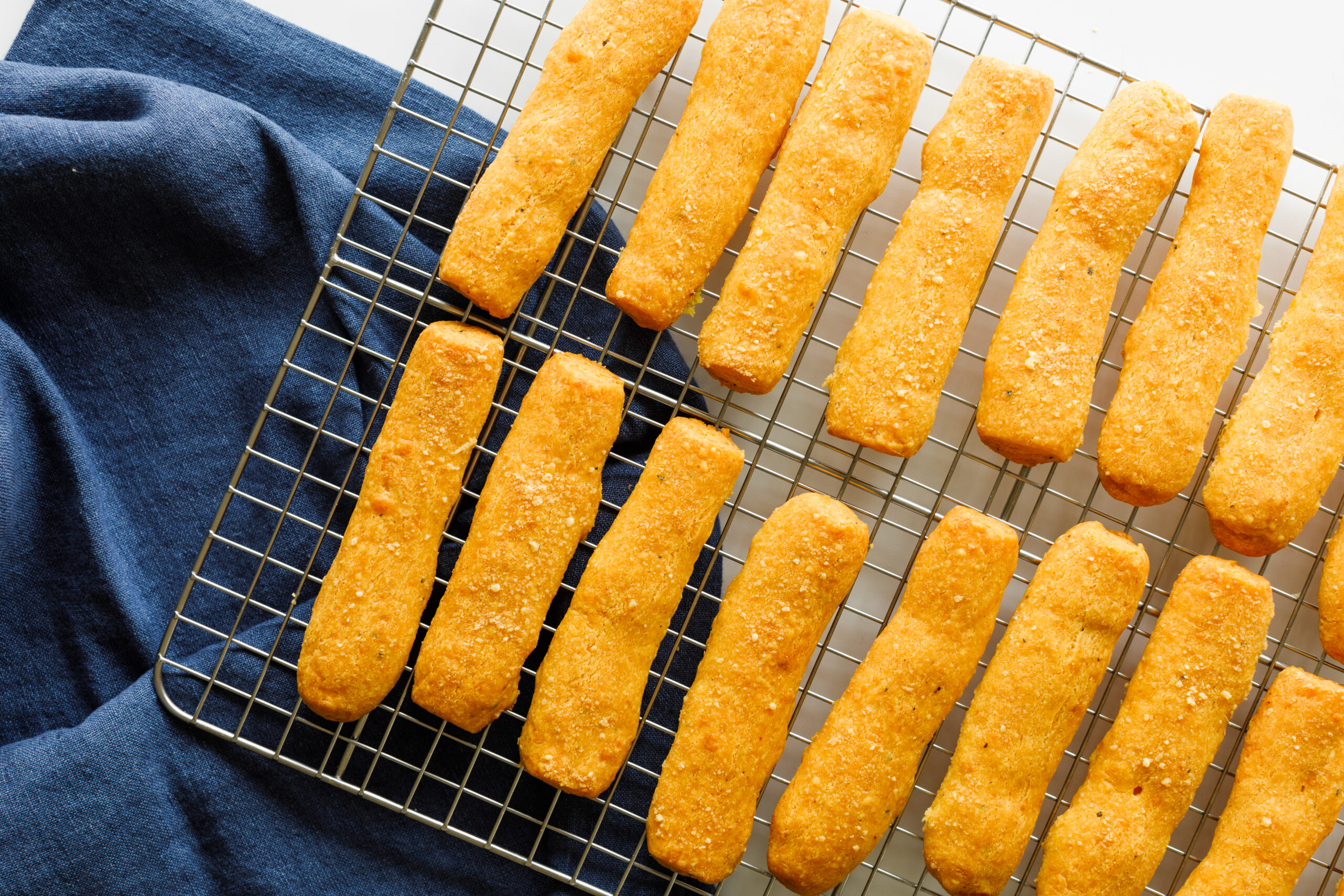 The finished cheese sticks on a cooling rack on top of a blue tablecloth.