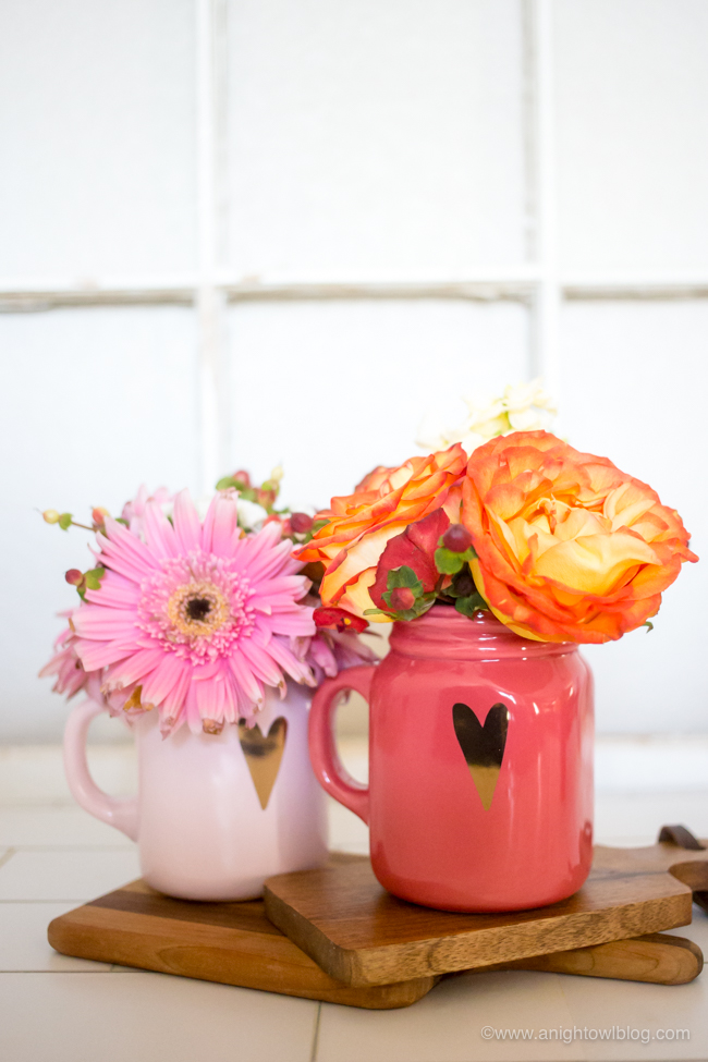 Two mugs with hearts with flowers arranged in it.