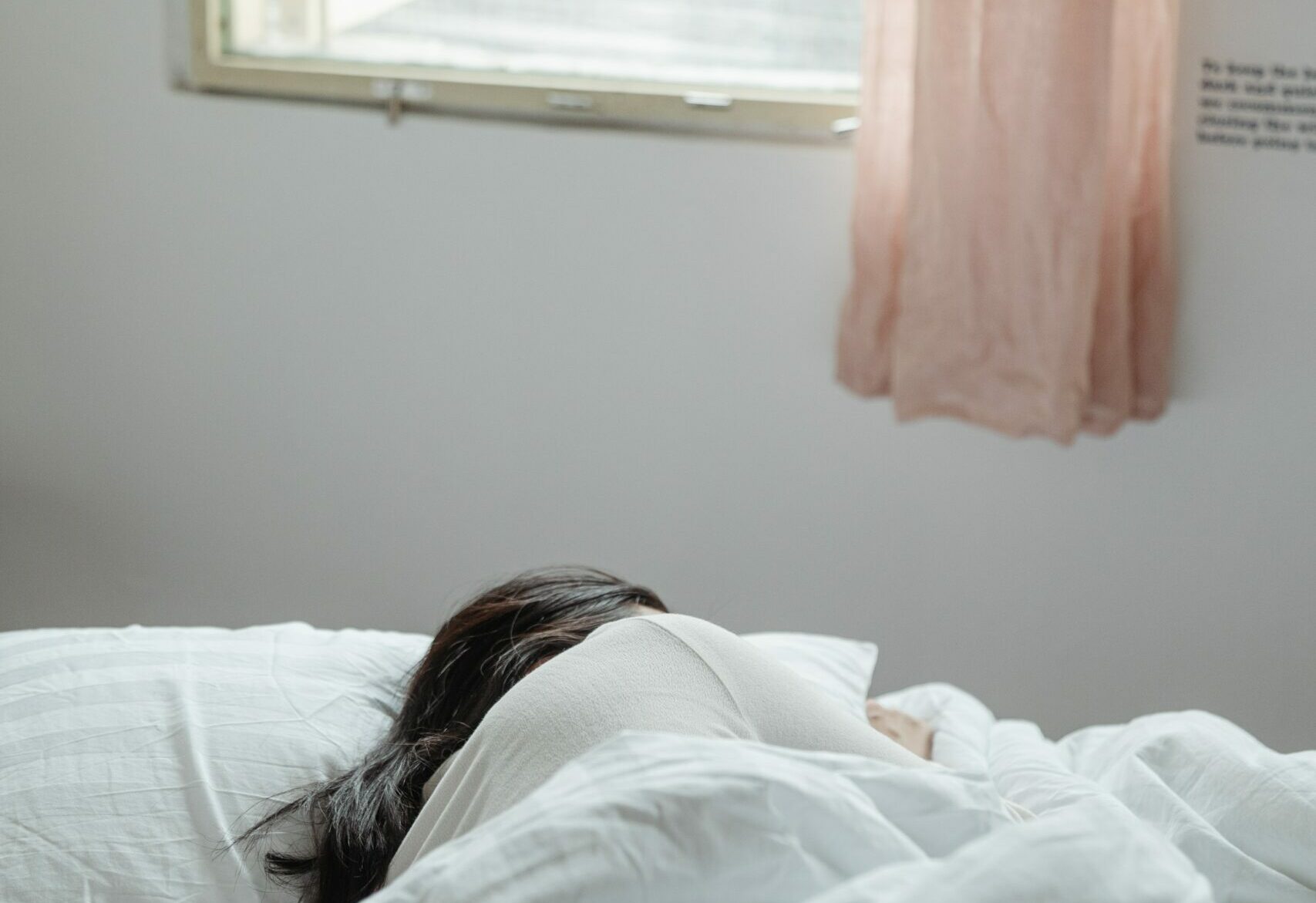 A woman sleeping on her side in a bed with light coming through a window - a way to treat insomnia naturally