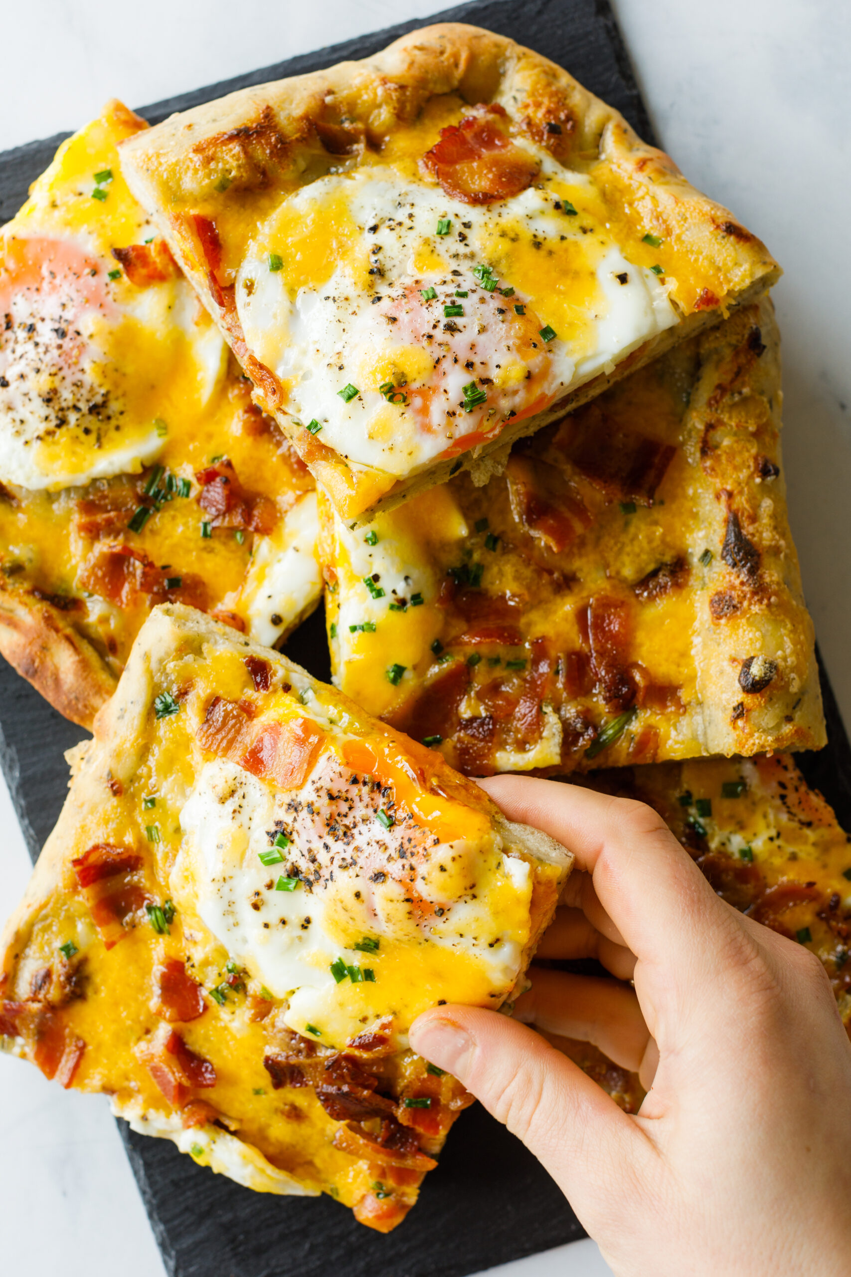 A handful of pizza slices with a handing lifting one up.