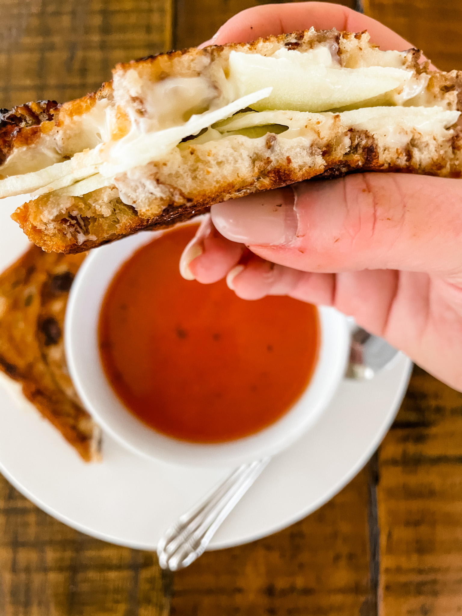 Marie holding the Grilled Apple and Brie Cheese Sandwiches above a bowl of tomato soup