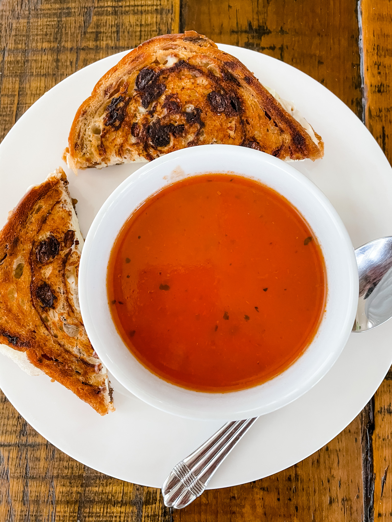 A cut in half Grilled Apple and Brie Cheese Sandwiches placed next to the bowl of tomato soup