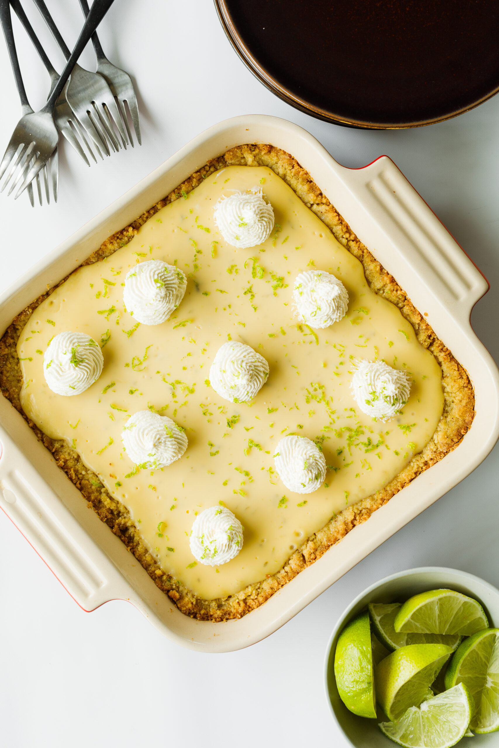The Key Lime Pie Bars, surrounded by forks, slices limes, and serving plates