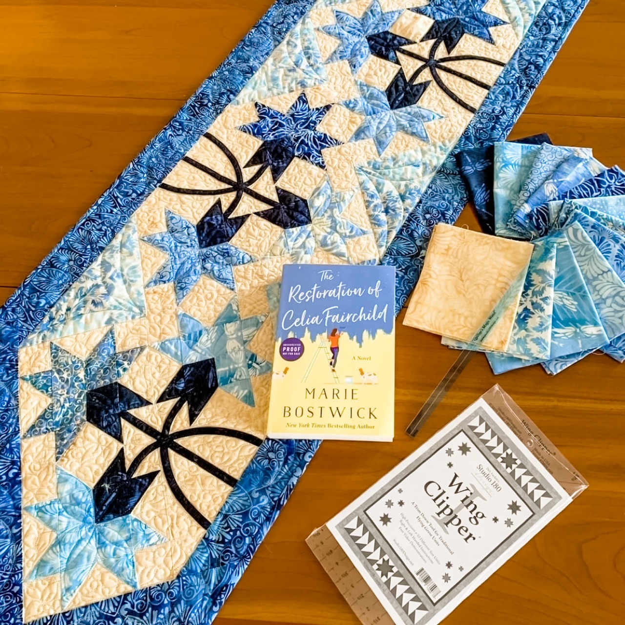 The quilted table runner with Marie's novel and fabric swatches surrounding it. 