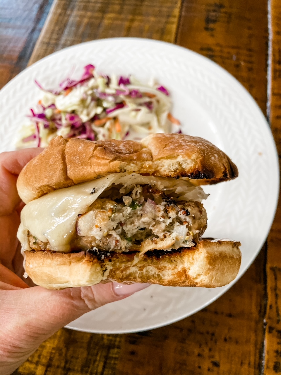 Marie's hand holding a Chicken Rueben Burgers with a bite taken from it