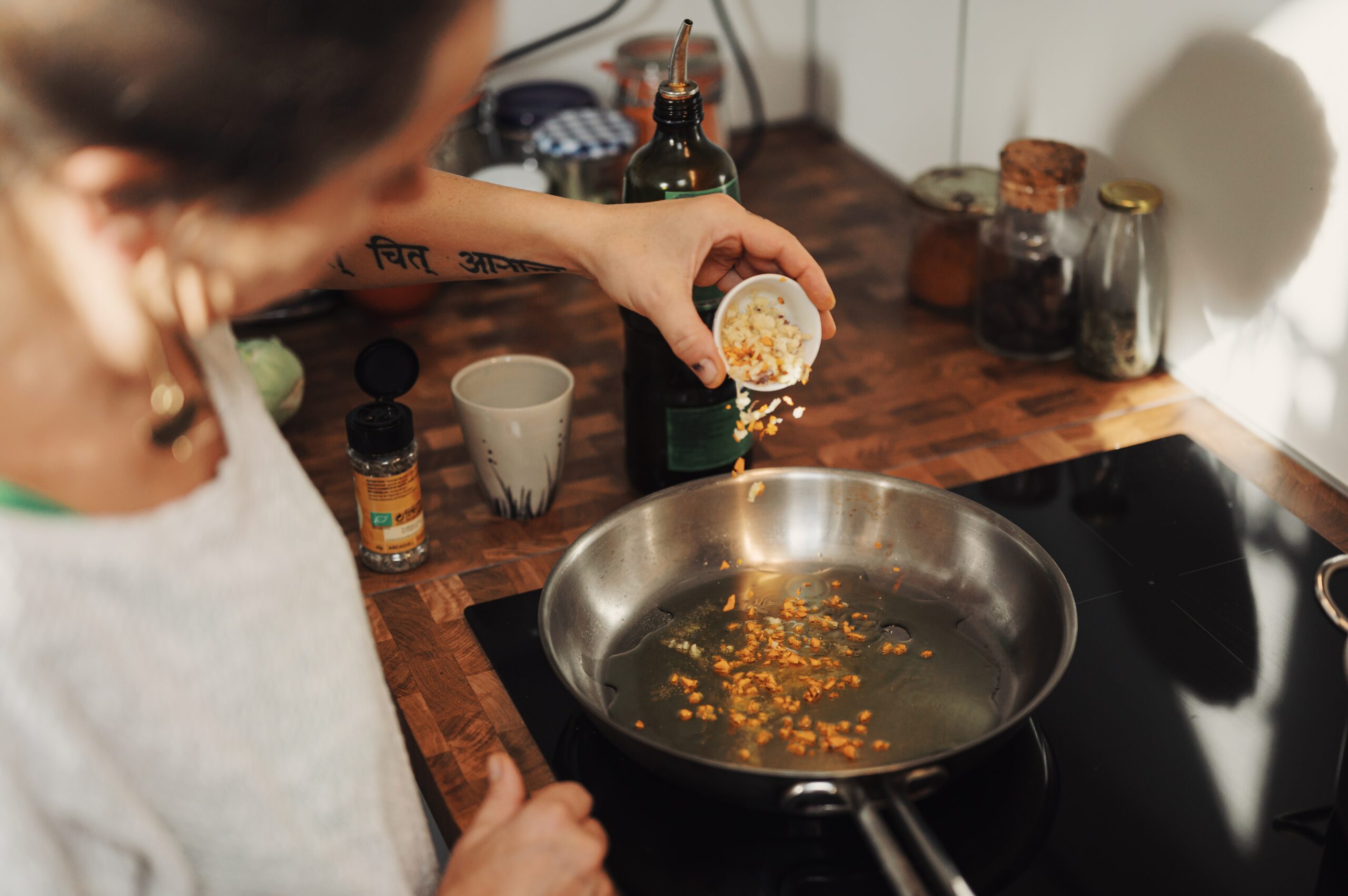 An older woman sprinkling pine nuts into a pan.
