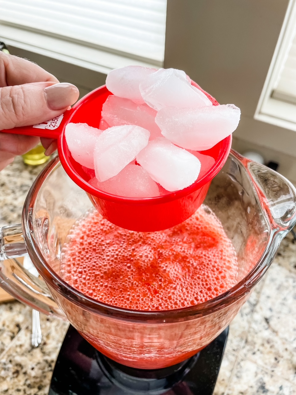 Marie holding a cupful of ice over the mixture-filled blender