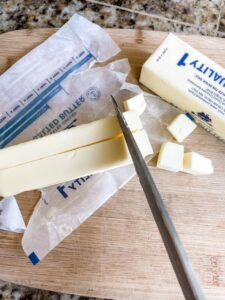 A stick of butter being sliced into small cubes on top of a cutting board