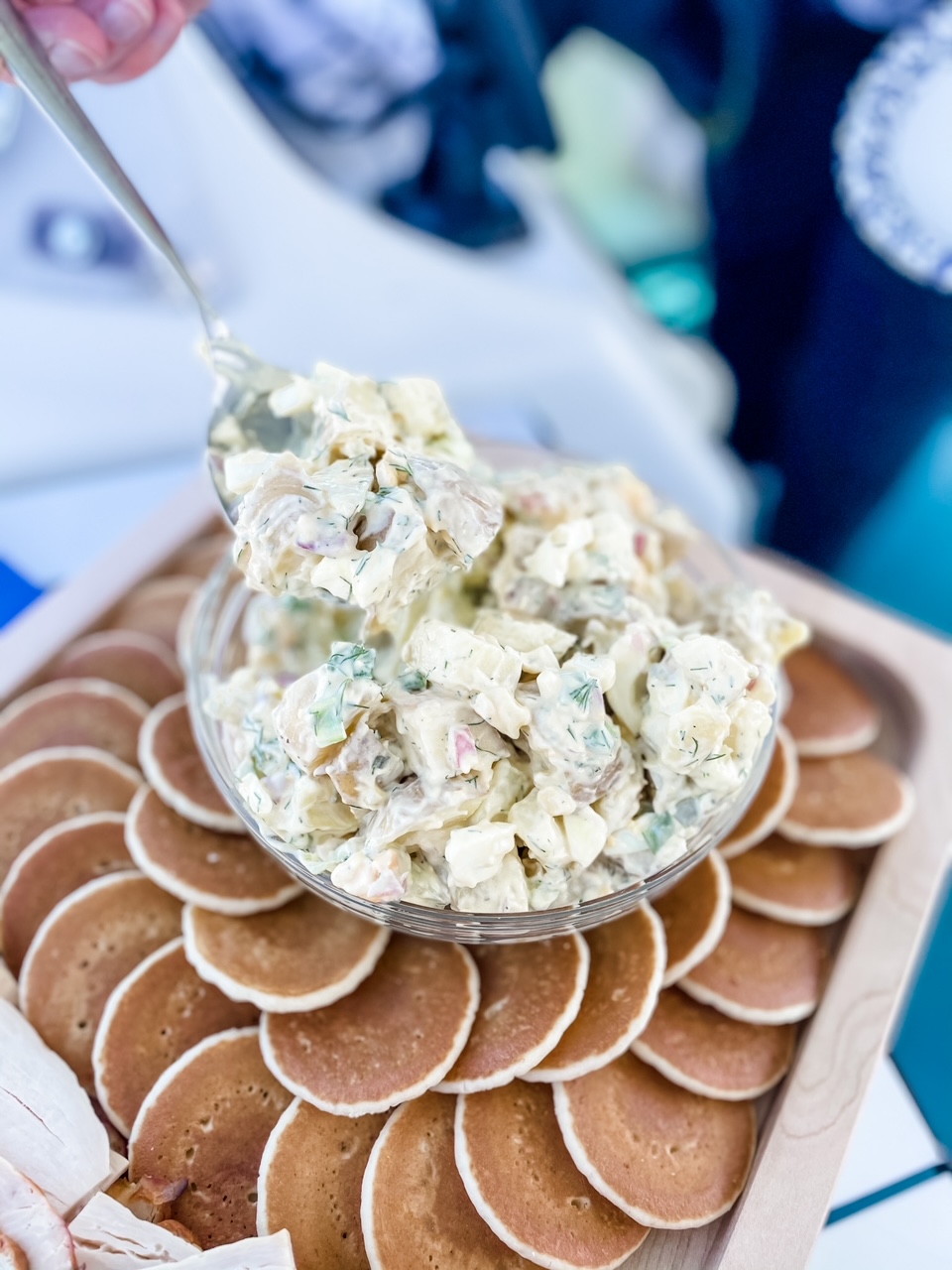 A bowl of the Potato Salad with Dill surrounded by small pancakes on a serving dish