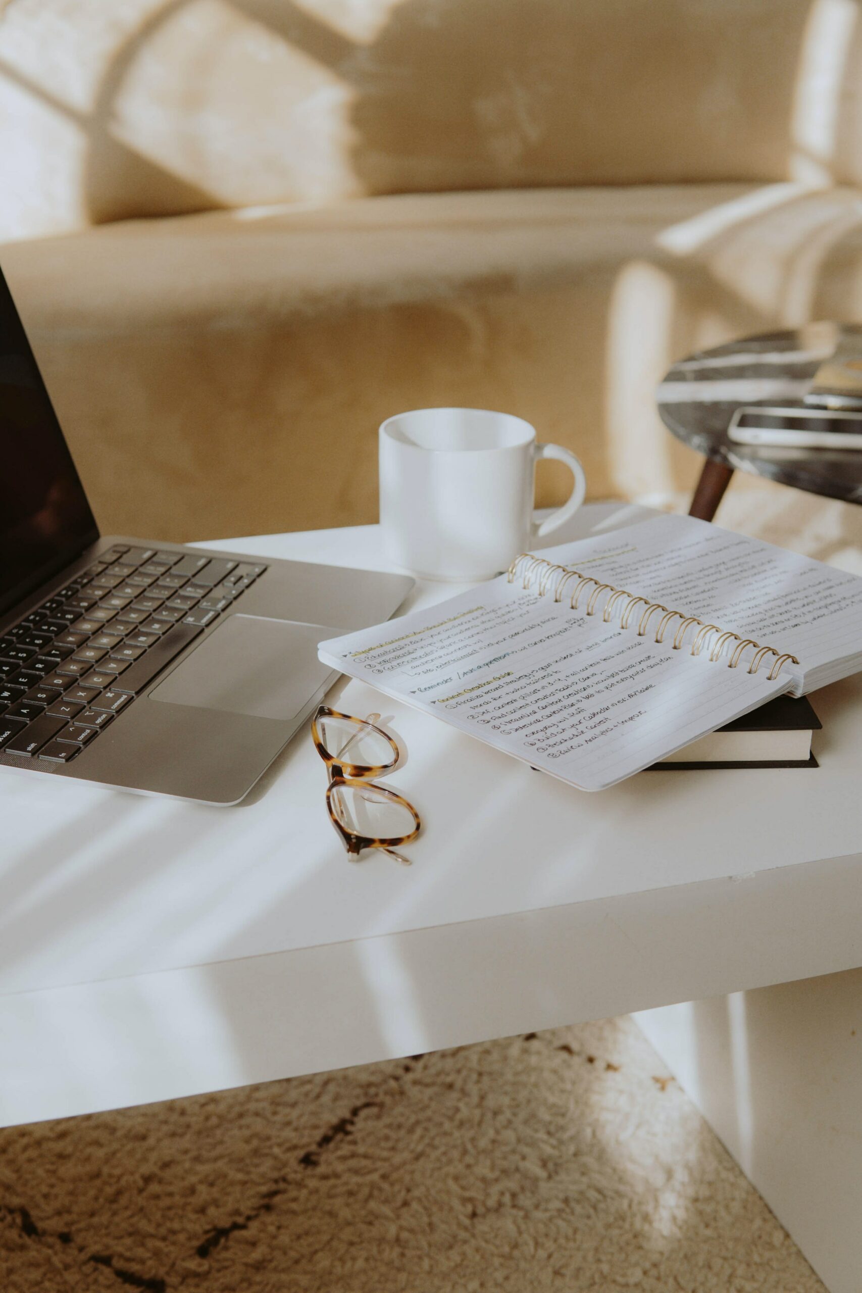 A table with a laptop, glasses, mug, and notebook