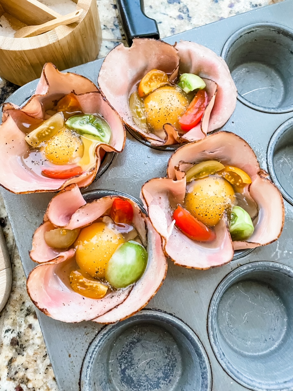 The muffin tin lined with ham and filled with the egg mixture