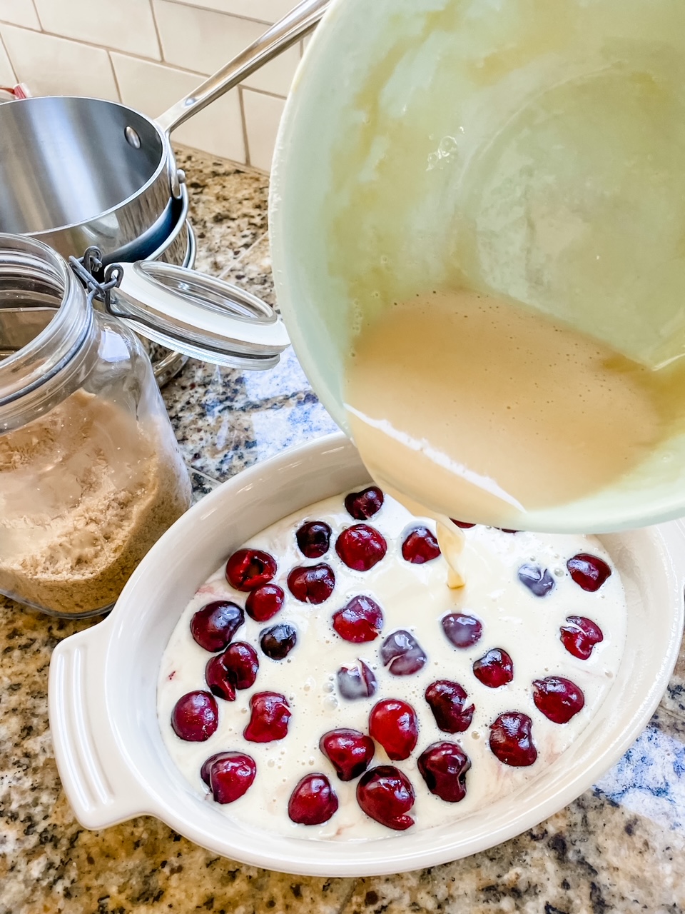 The batter being poured over the baking dish filled with cherries