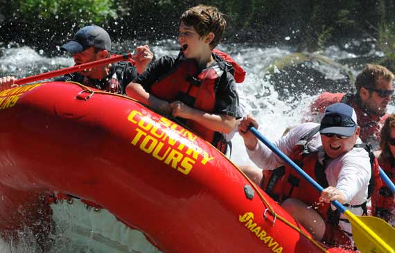 A Sun Country Tour raft filled with passengers with oars and wearing life vests