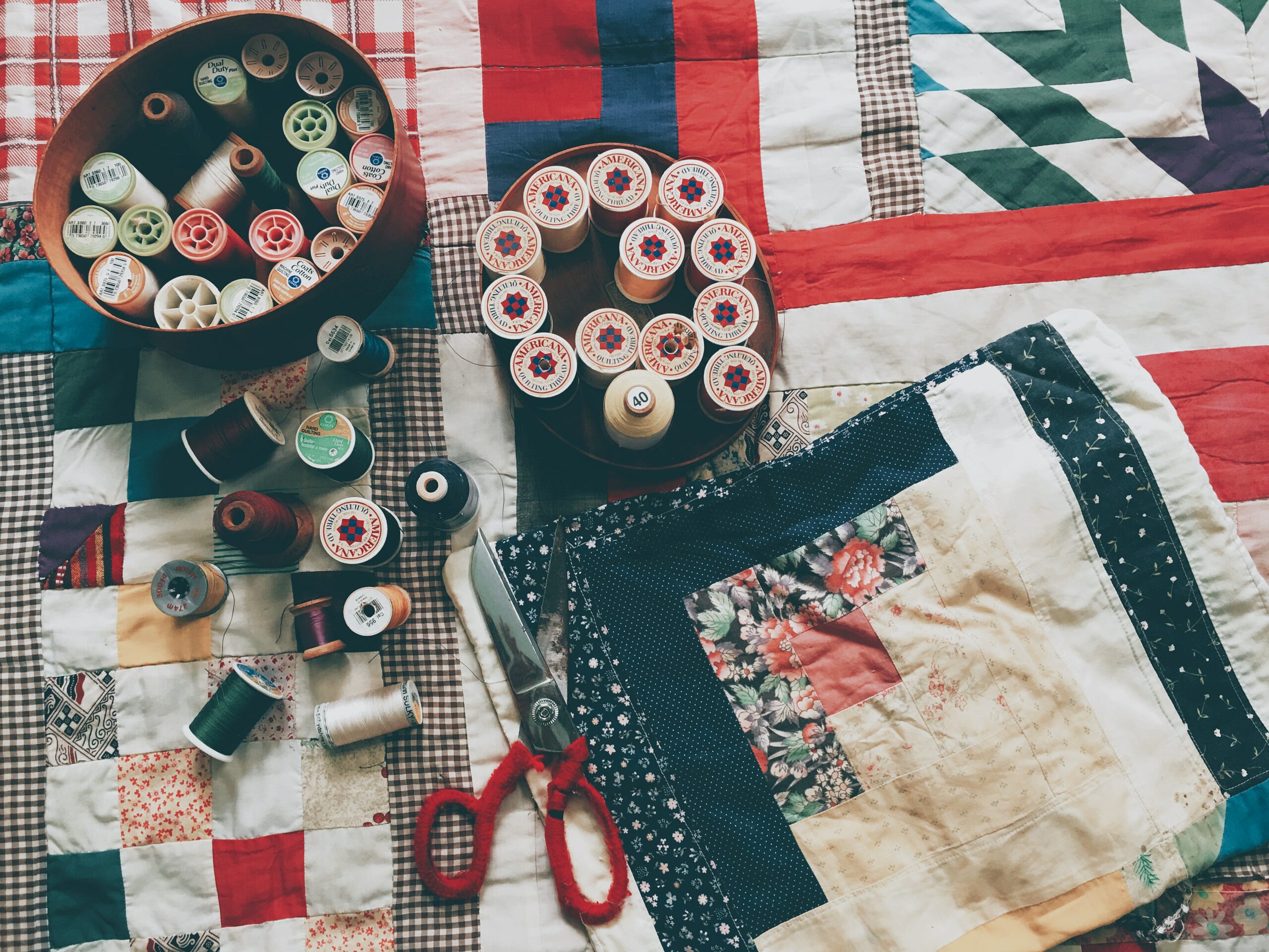 Threads, sciccors, and other equipment laid ontop of a quilt