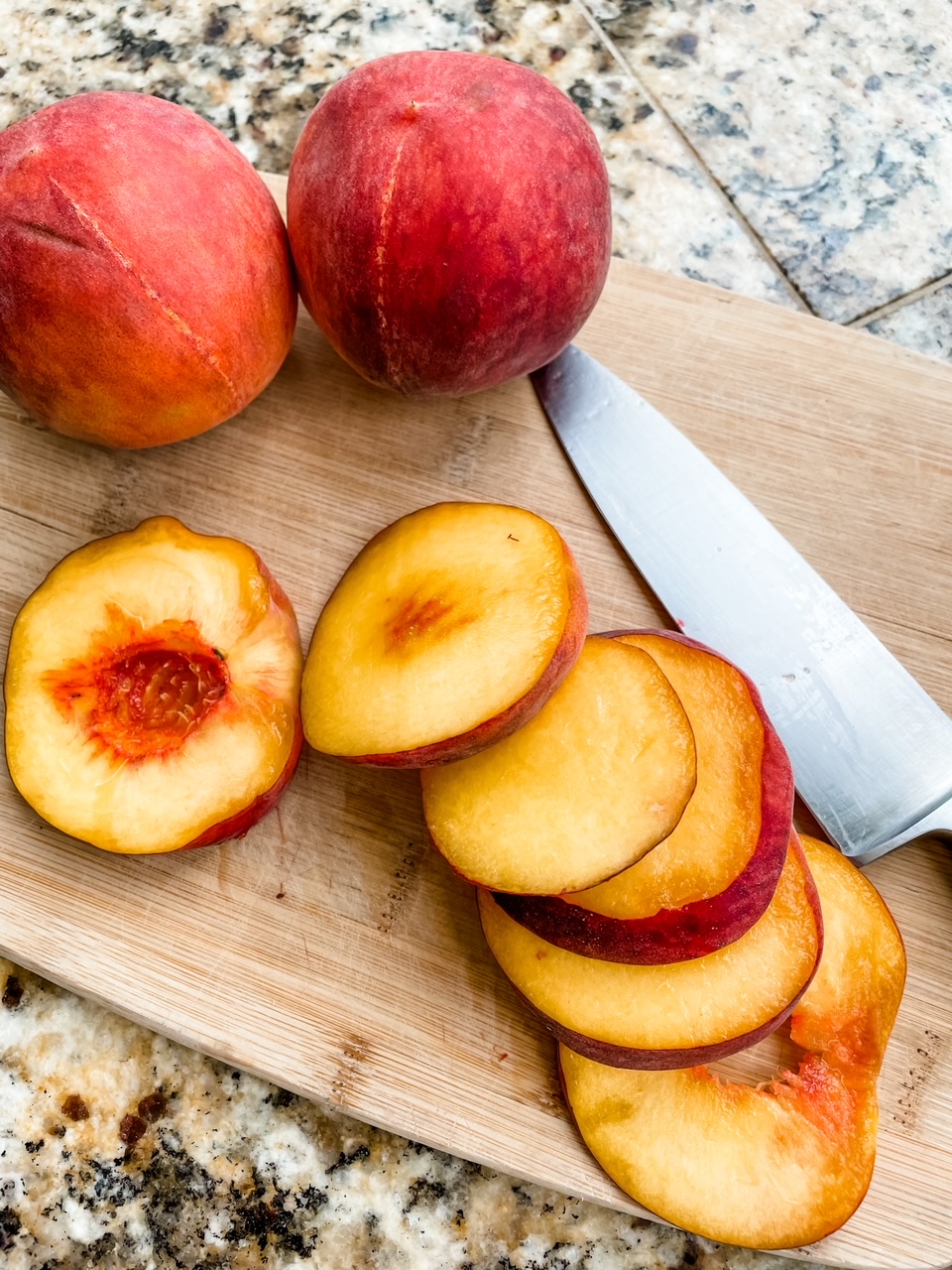 Two whole peaches and a sliced one on a cutting board