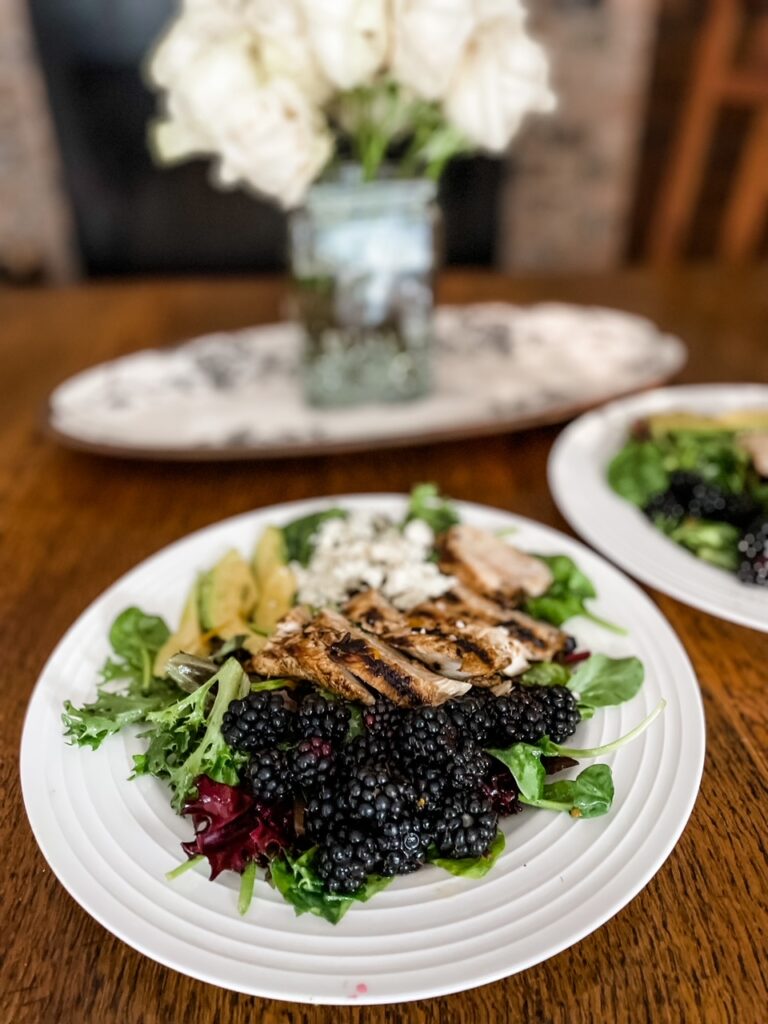 A dining table set with flowers and two plates of Marie's Blackberry and Grilled Rosemary Chicken Salad