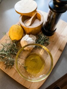 The ingredients for the Blackberry and Grilled Rosemary Chicken Salad on a wooden cutting board - oil, pepper, rosemary, orange, garlic.