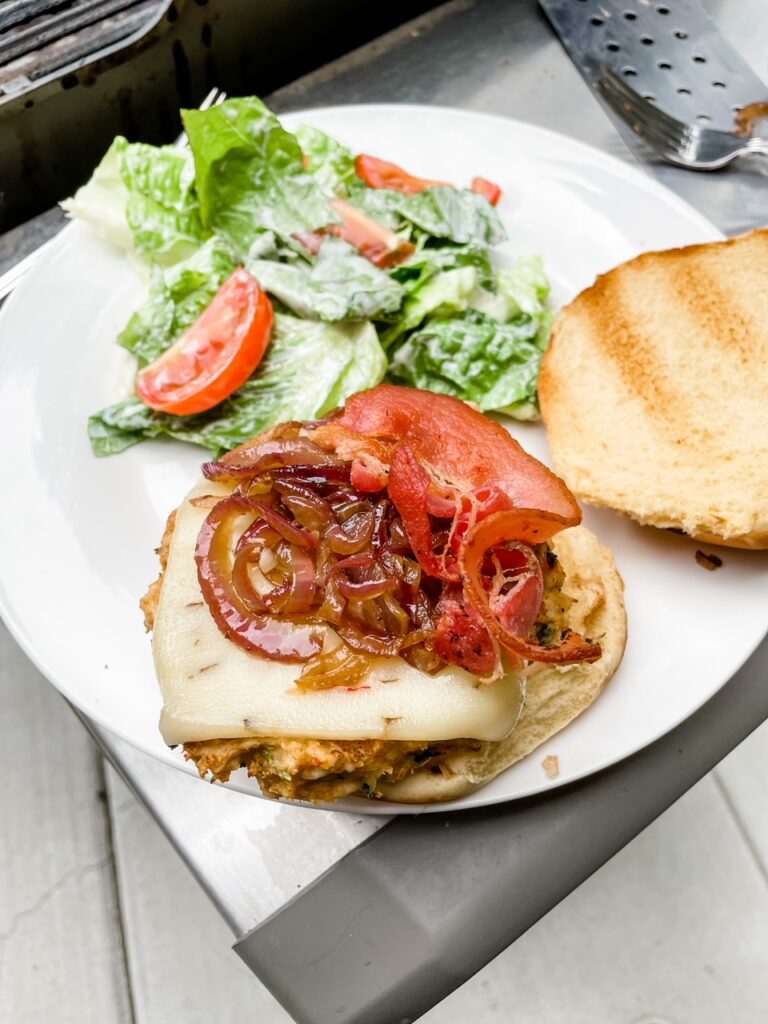 The finished Chicken Bacon Burgers with the top bun taken off, showing the red onion on top