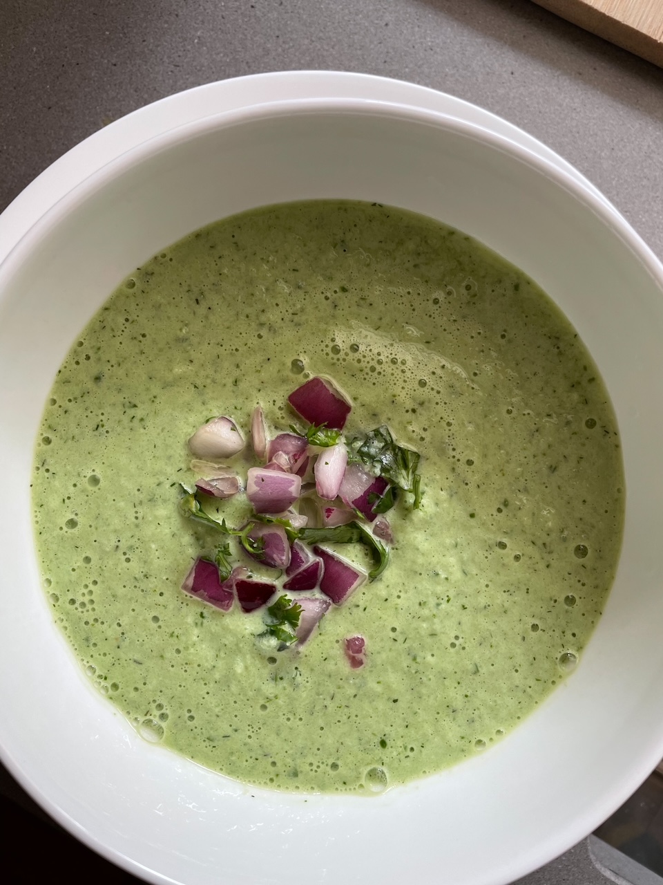 A bowl of the Cold Cucumber Soup garnished with chopped red onions