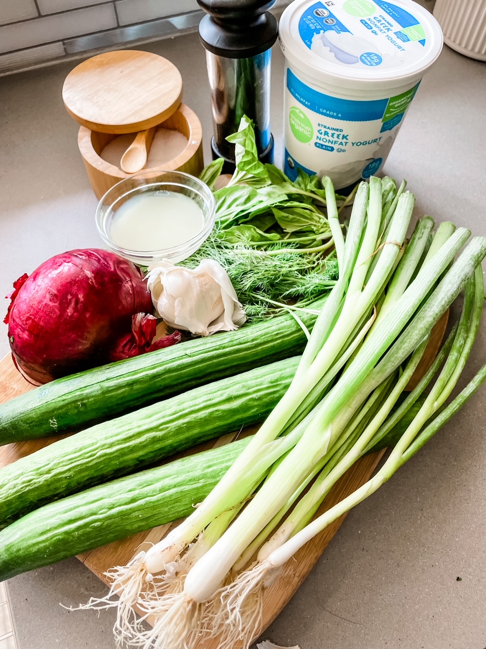 The ingredients for the Cold Cucumber Soup laid out on a countertop - cucumbers, green onion, greek yogurt, red onion, salt, and pepper