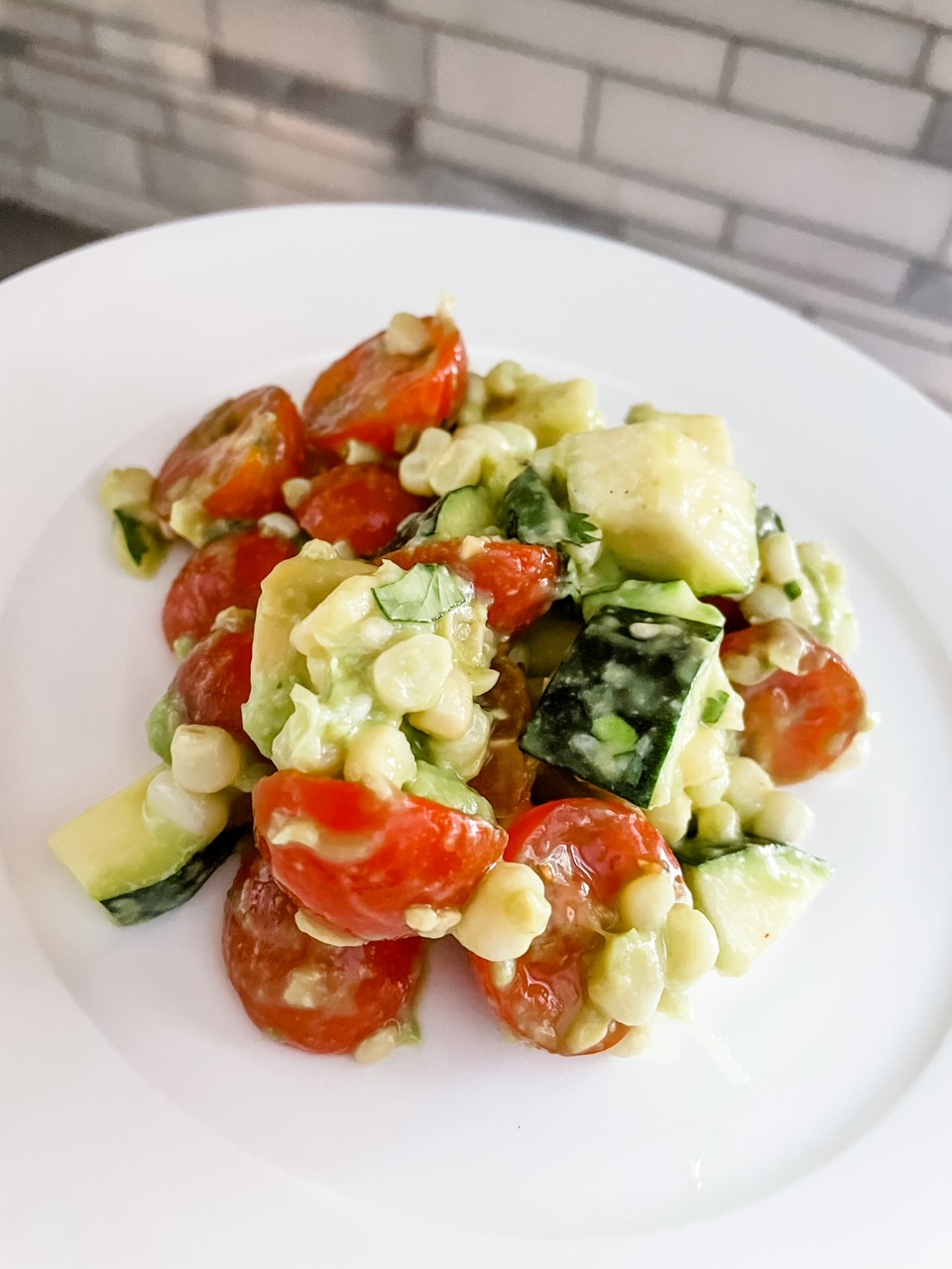 A serving of the Corn and Zucchini Salad with Avocado Dressing on a white plate