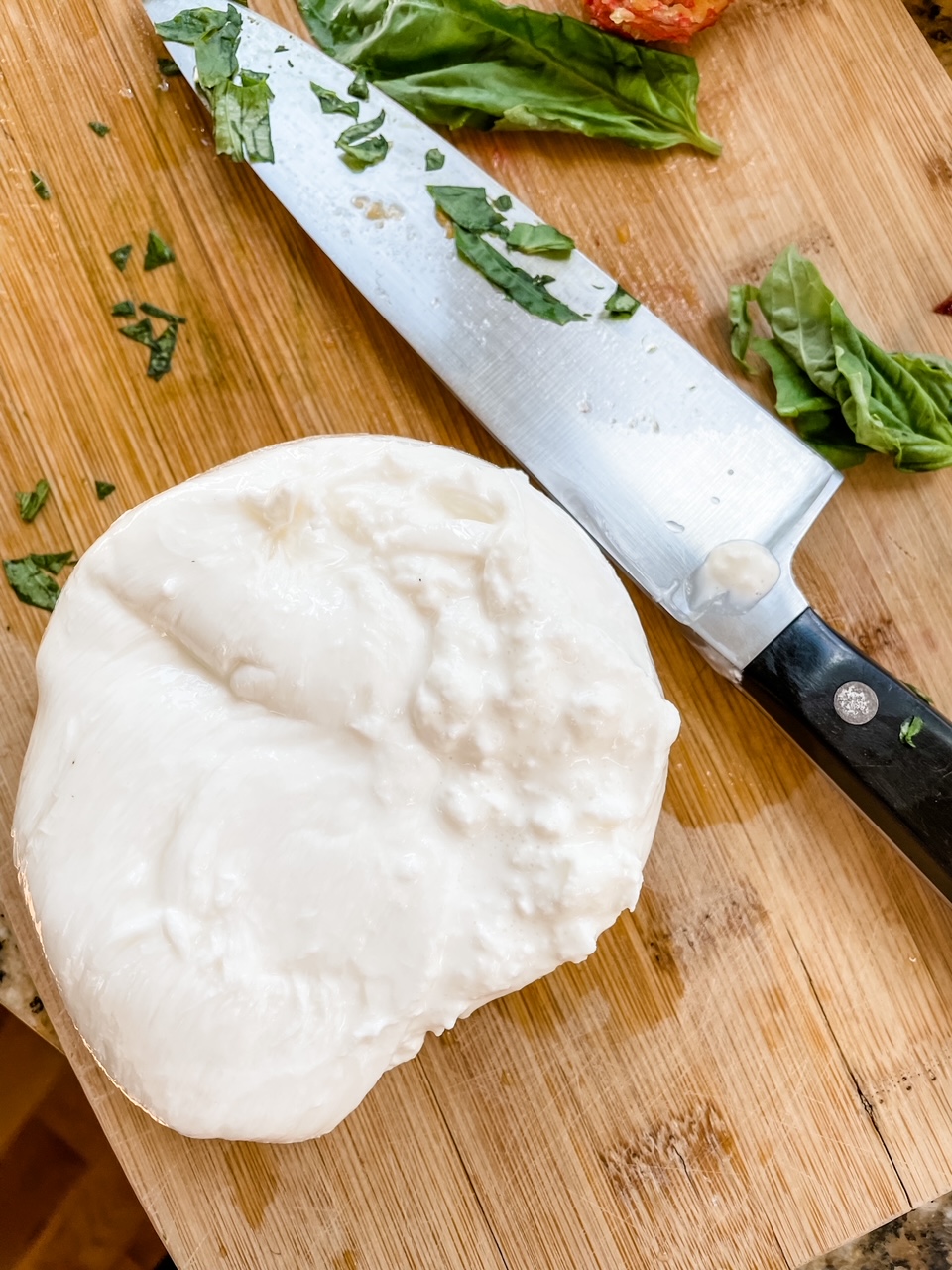 A hunk of burrata, sliced in half, next to a knife on a cutting board