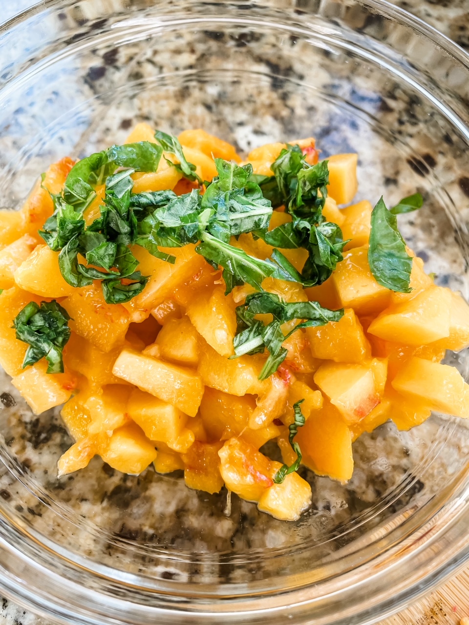 A clear bowl filled with sliced pieces and chopped basil leaves