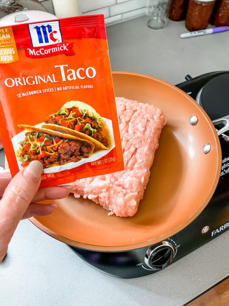 Marie holding up a packet of McCormick Seasoning above a pan filled with ground chicken