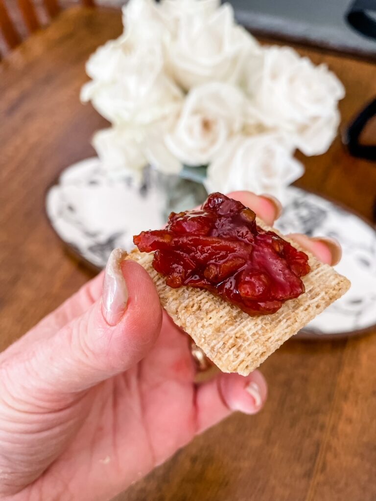 A cracker being held up with some of the Easy Tomato Jam with Maple spread on it
