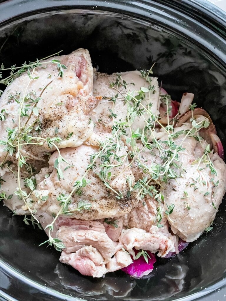 The raw chicken with thyme in a slow cooker
