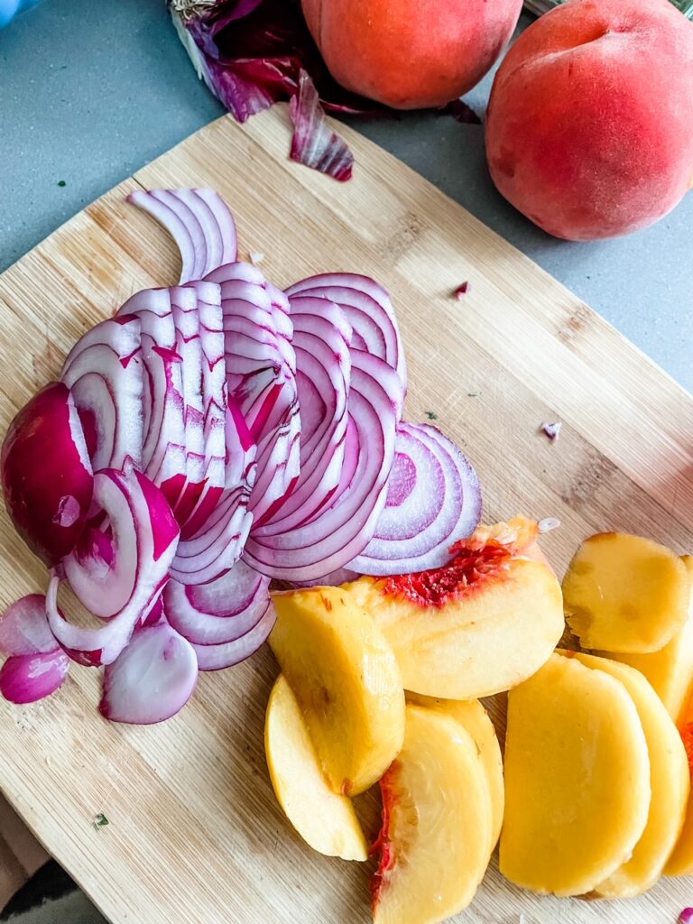 Sliced red onion and peaches on a wooden cutting board