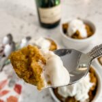 The Slow Cooker Pumpkin Bread Pudding served in three small white bowls with a spoon holding up a scoop of one