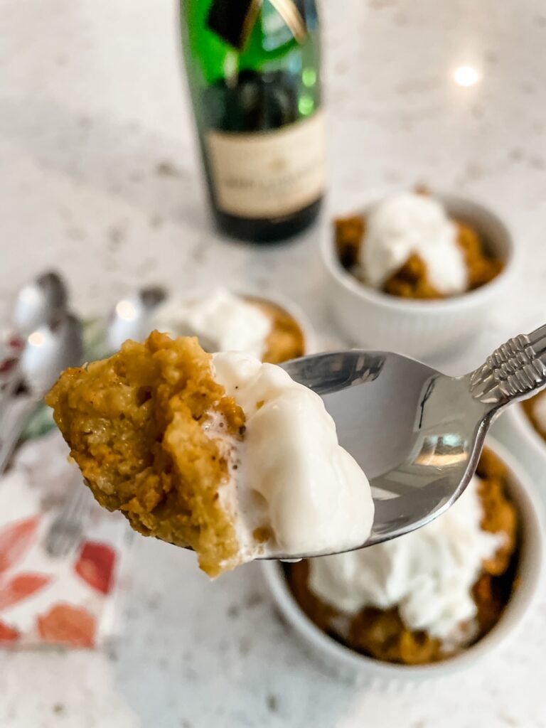 The Slow Cooker Pumpkin Bread Pudding served in three small white bowls with a spoon holding up a scoop of one