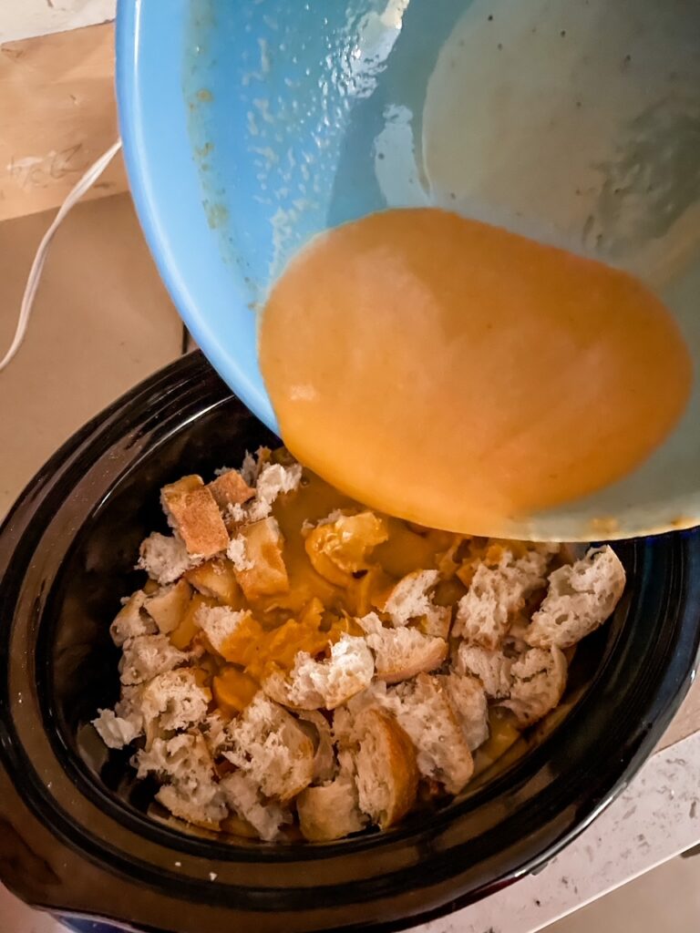 The wet ingredients for the pudding being poured on top of the torn bread chunks.