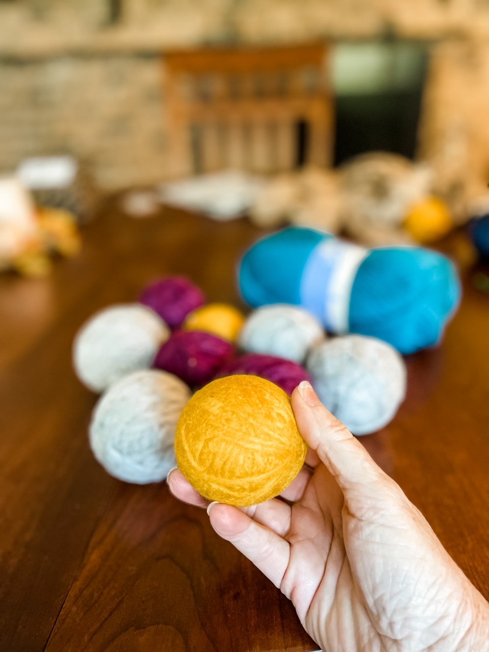 A hand holding up a yellow ball in front of several other DIY Yarn Dryer Balls on a table