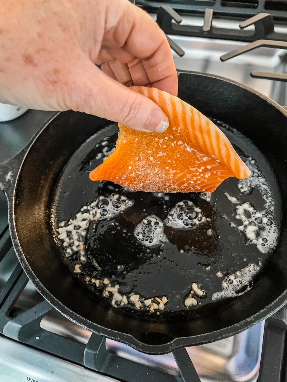 Marie's hand placing th piece of steelhead trout into a cast iron pan