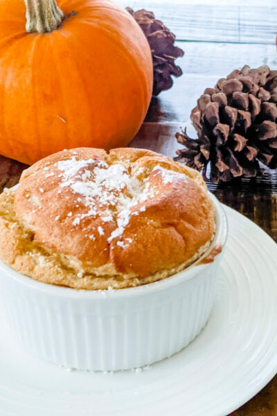 The pumpkin soufflé on a plate with pumpkin and pinecone in the background