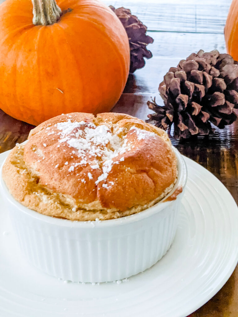 The pumpkin soufflé on a plate with pumpkin and pinecone in the background