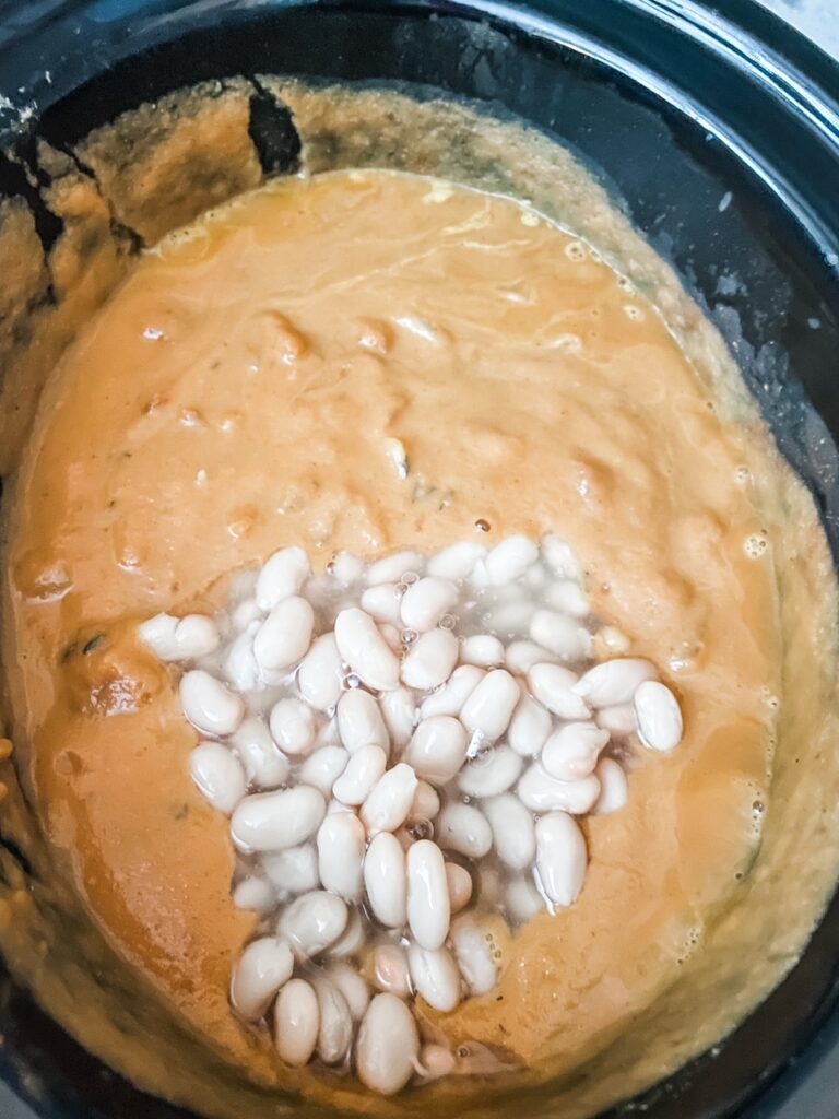 Marie adding the white beans into the slow cooker, already filled with the rest of the ingredients for the Vegan Crock Pot Pumpkin Soup with White Beans