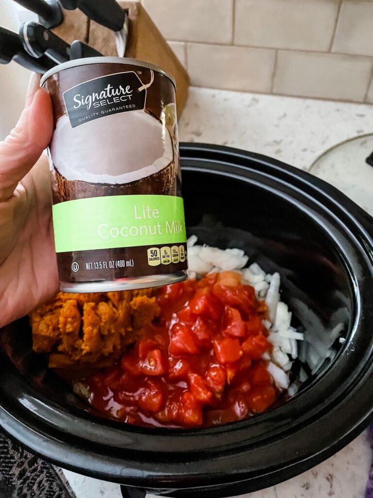 Marie holding the lite coconut milk above the crock pot, filled with chopped onions and diced tomatoes