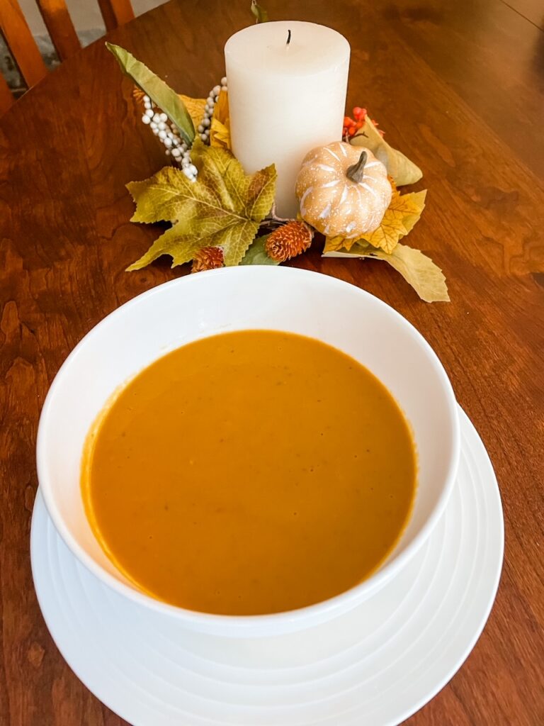 A bowl of the finished Vegan Crock Pot Pumpkin Soup with White Beans with a candle wreath behind it