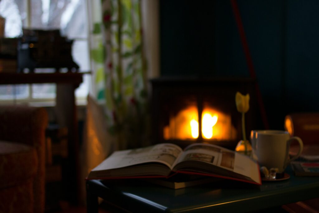 A living room with a fireplace, books, and an open window on a rainy evening