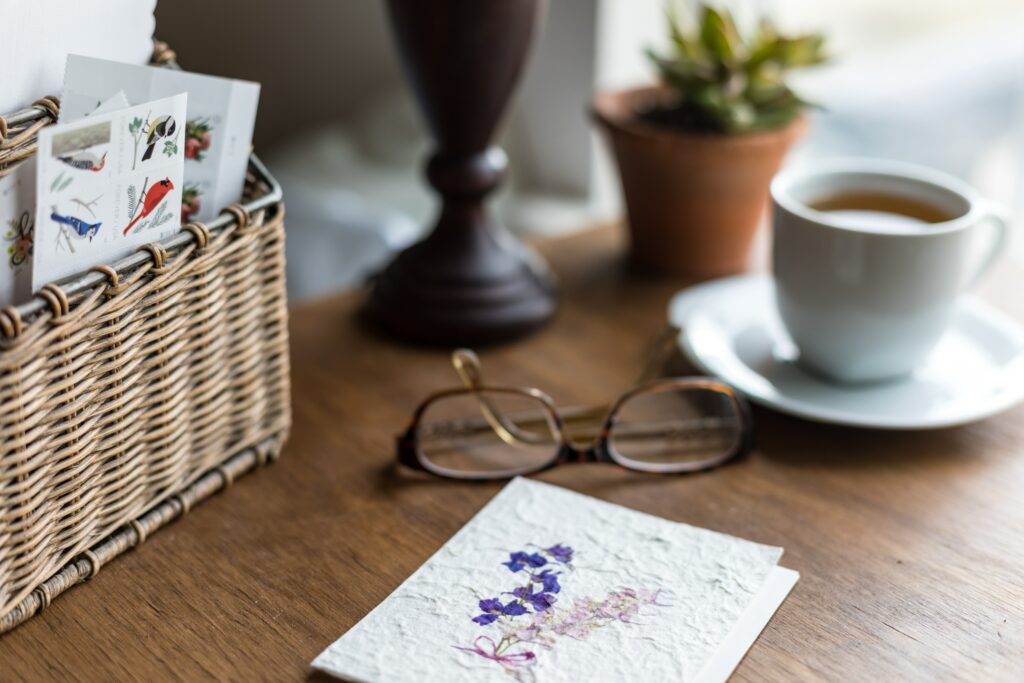 A basket of cards and a finished letter next to a pair of glasses and cup of tea