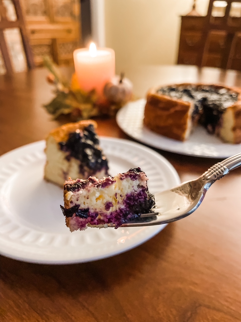 A fork carrying a piece with the Blueberry Greek Yogurt Cheesecake slice behind it