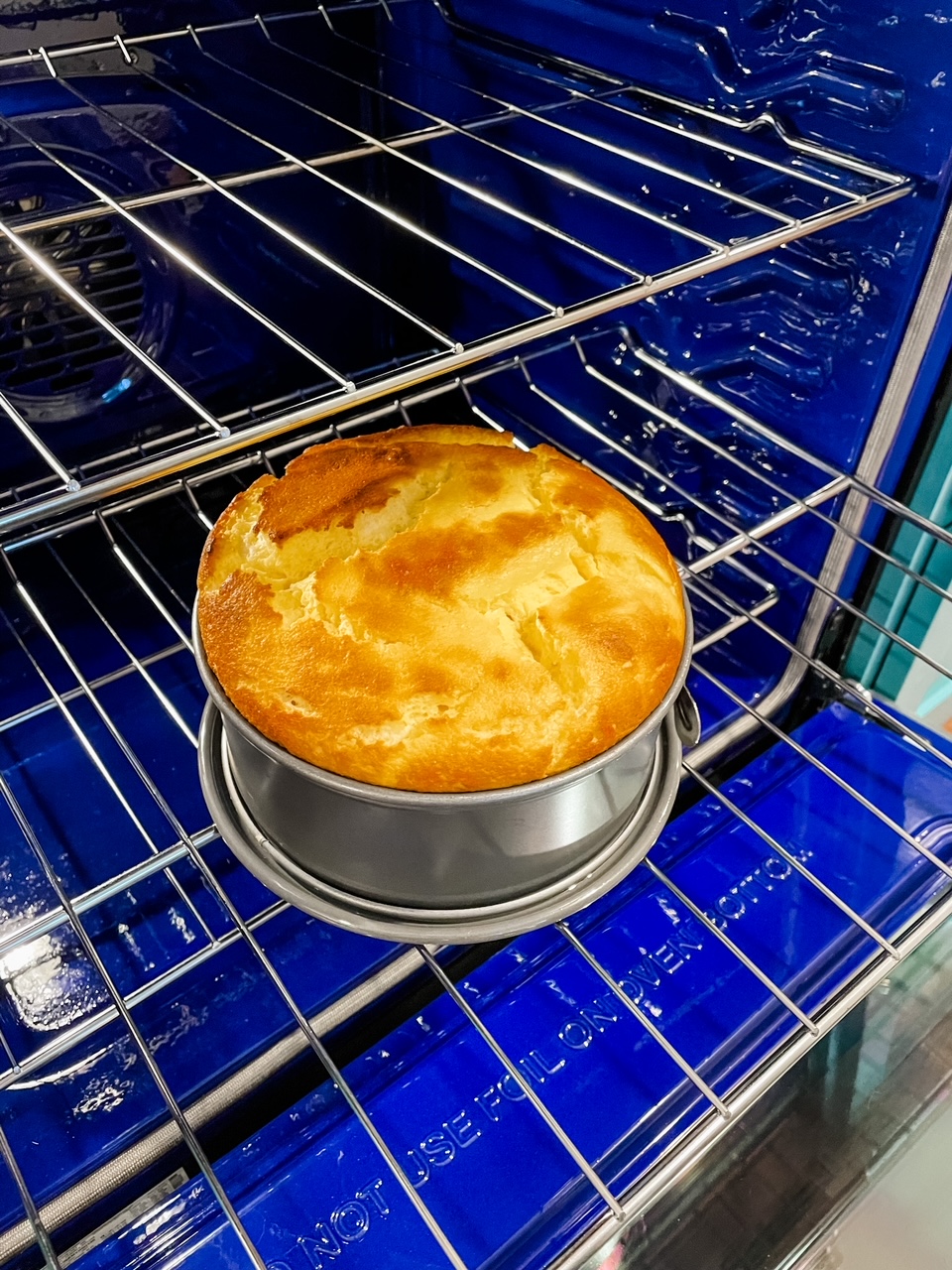 The baked cheesecake being pulled out of the oven with the proper golden top