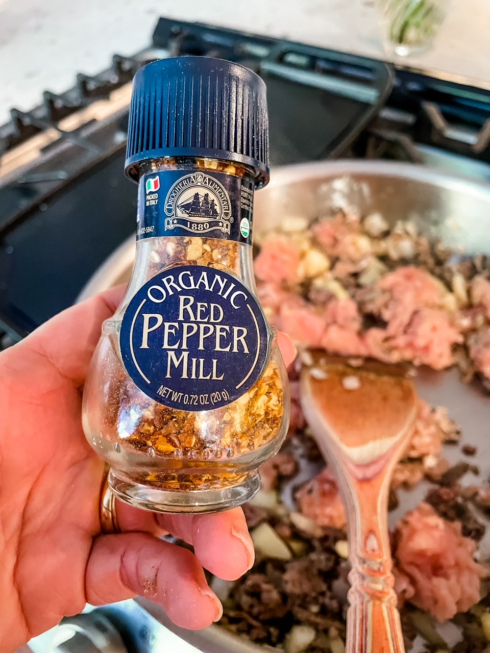 A Red Pepper Mill held above the pan full meat