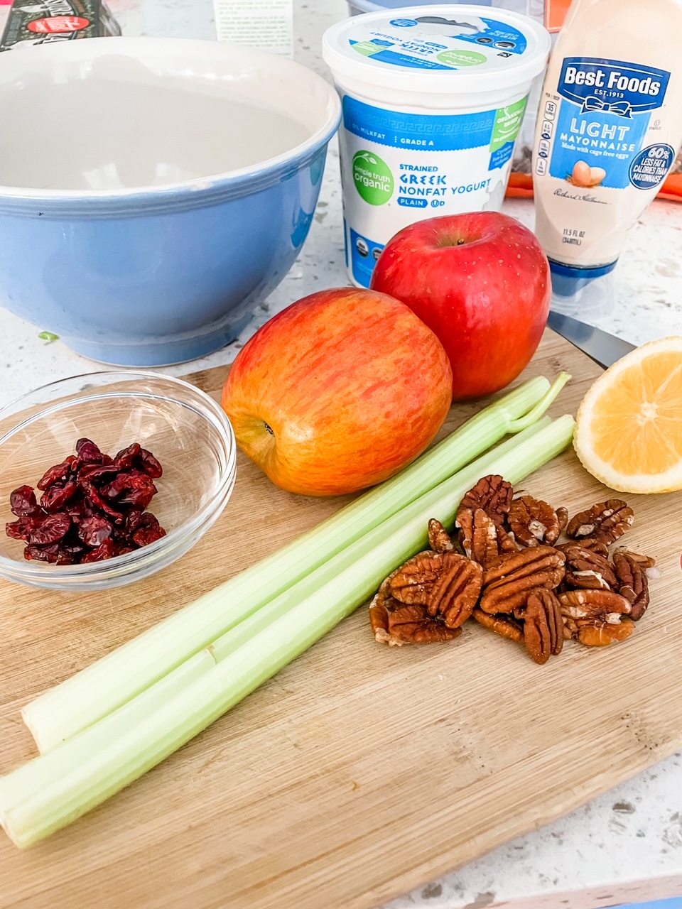 The ingredients (apples, craisins, orange, celery, and greek yogurt) on a cutting board