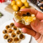 A hand holding up one of the Apricot, Cherry, and Brie Filo Pastry Tarts above the platter of finished ones