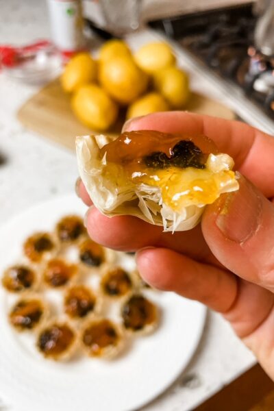 A hand holding up one of the Apricot, Cherry, and Brie Filo Pastry Tarts above the platter of finished ones