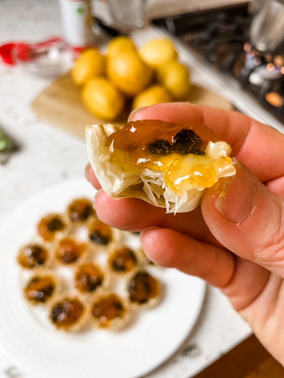 A hand holding up one of the Apricot, Cherry, and Brie Filo Pastry Tarts above the platter of finished ones